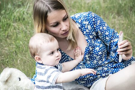 Beautiful mather and a baby boy sitting on grass and looking at electronic deviceの写真素材