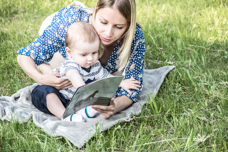 Beautiful happy mather with baby boy reading a book outdoor on the meadowの写真素材