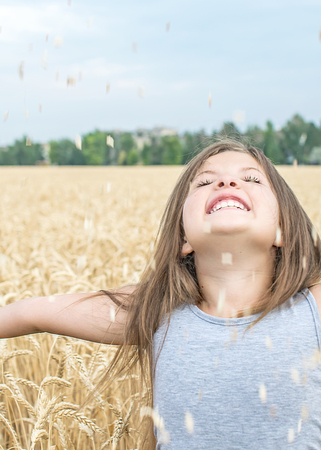 Laughing little girl throws up wheat grains. Concept of purity, growth, happinessの写真素材