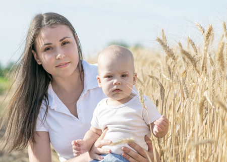 Young pretty mother with her adorable baby boy sitting in wheat field at summer dayの写真素材