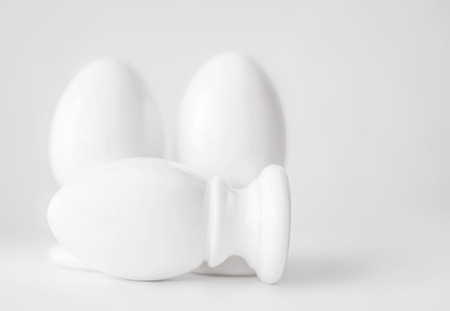Group of three white ceramic eggs on stands or in egg-cups on white blurred background. Easter religious Christian symbol. Monochrome image. Interior church decoration.の写真素材