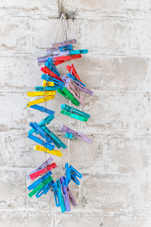 Cororful or multi-colored plastic clothespins on rag rope on rusty nail on white old brick wall background.の写真素材
