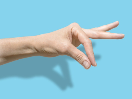 Female hand isolated on blue background with shadow. The thumb and forefinger are assembled into a...