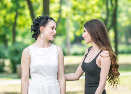 Portrait in profile of two young beautiful women friends talking in green summer park. Pretty females Bride and bridesmaid smiling and looking at each otherの写真素材