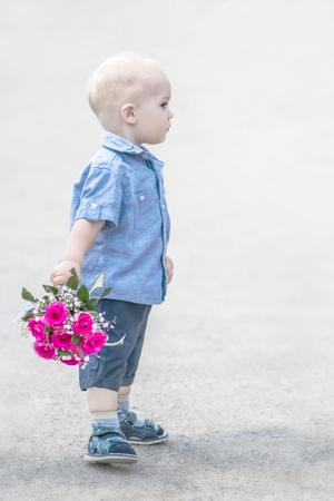 Portrait half-face of small baby boy standing with pink roses bouquet outdoor.の写真素材