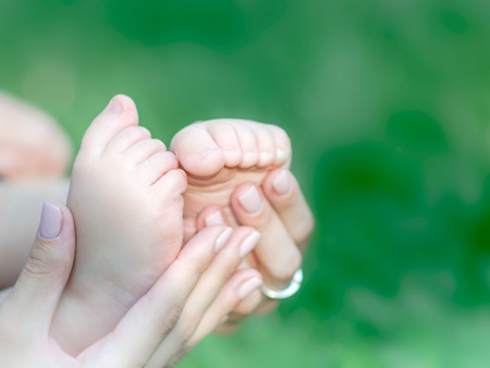 Mother holding feet of newborn baby on green grass background. The concept of maternal tenderness, care, love and health. Copy space.の写真素材