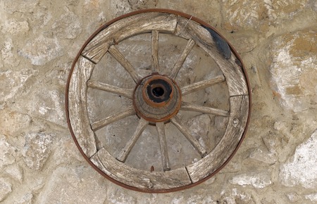 Old vintage wooden wheel hanging on a stone wall of a house