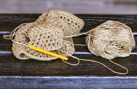Yellow metal crochet hook and unfinished knitting left by knitter on wooden benchの写真素材