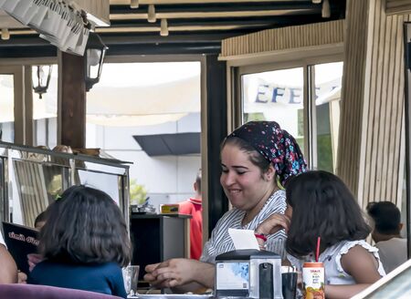 CYPRUS, NICOSIA - JUNE 10, 2019: Young smiling mother in traditional clothes enjoy a meal with two little daughters in open summer city cafe. Eating familyのeditorial素材