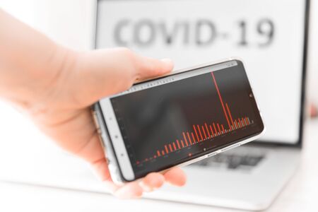 Person's hand holding mobile device showing schedule of growth of infected people. Breaking news on mobile phone highlighting total virus infected. World Pandemic 2020.の写真素材