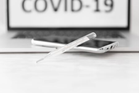 Laptop screen with the inscription Covid-19, medical thermometer and smartphone lying on keyboard....