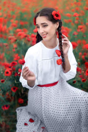 Portrait of a pretty young woman on the background of a blooming poppy field. Smiling Ukrainian...