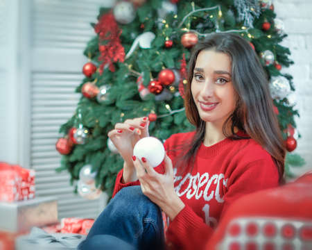 Happy young brunette female decorating christmas tree. Girl holding a christmas ball in her handsの写真素材