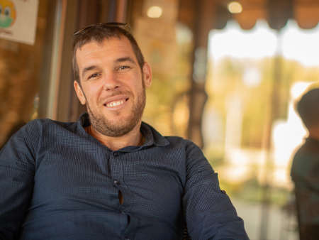 Close-up portrait of young smiling man sitting in cafe and looking into cameraの写真素材