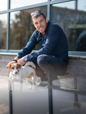 Portrait of smiling young man and small cute purebred dog jack russell terrier together on city...