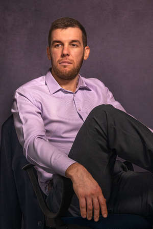 Portrait of a young handsome male businessman sitting in armchair in officeの写真素材