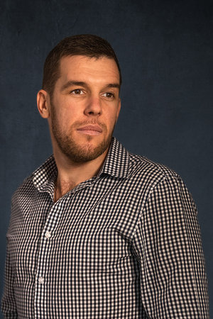 Close-up shoulder portrait of a young handsome man dressed in a plaid shirt standing against a dark background.の写真素材
