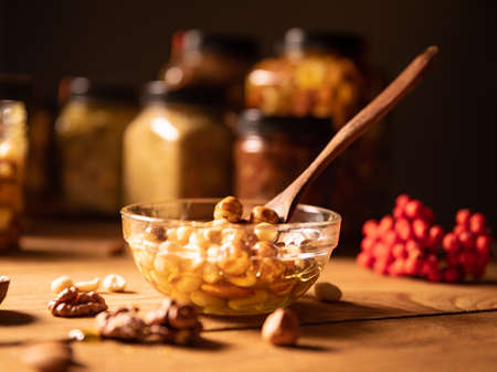 Honey mixed with nuts, seeds in a transparent plate with a wooden spoon, jars of honey and a branch...