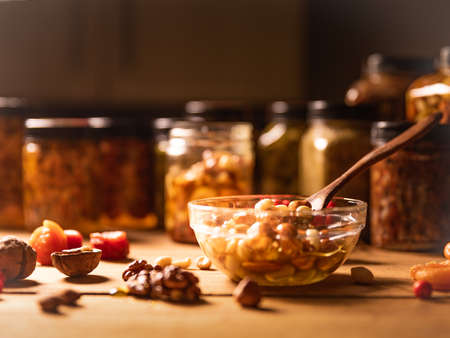 Farmer Honey mixed with nuts, seeds in a transparent plate with wooden spoon, jars, walnuts, dried apricots on rustic wooden kitchen table. Still life photographyの写真素材