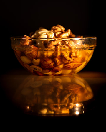 Honey mixed with nuts in round bowl on table with reflection on black background. Still life photography.の写真素材