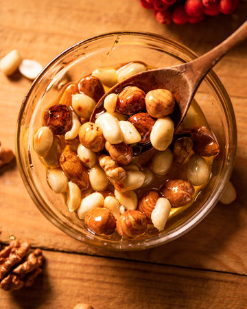 Top view of round bowl with Honey mixed with nuts, rowan berries and peeled walnuts on wooden table....
