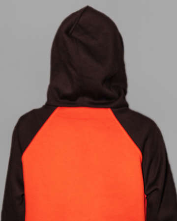 A man guy dressed in a orange and black hoodie with a hood on his head standing backwards.の写真素材