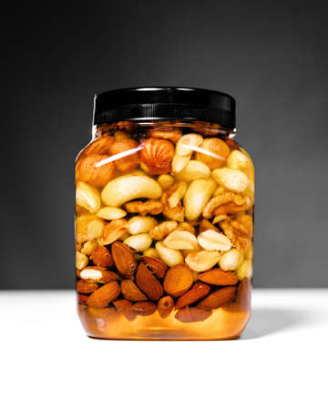 Jar of honey with nuts on white table on dark background.