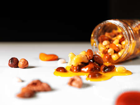 Closeup jar of honey mixed with nuts spilled on white table on black background.の写真素材