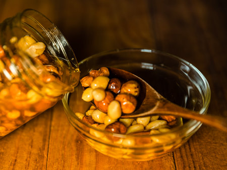 Farmer Honey mixed with nuts, seeds pouring from a transparent jar into a wooden spoon on glass plate on kitchen wooden table. Still life closeup photographyの写真素材