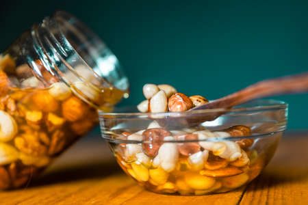 Farmer Honey mixed with nuts, seeds pouring from a transparent jar into a wooden spoon on glass plate on kitchen wooden tableの写真素材