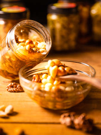 Honey mixed with nuts, seeds pouring from a transparent jar into a glass plate. Still life photographyの写真素材