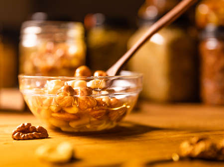 Honey mixed with nuts, seeds in a transparent plate with wooden spoon, one jar, walnuts kernel, red rowan, on rustic wooden kitchen table. Still life photography.の写真素材