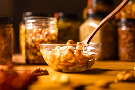 Honey mixed with nuts, seeds in a transparent plate with wooden spoon, one jar, walnuts kernel, red...
