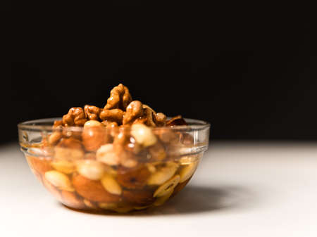 Honey mixed with nuts in round bowl on white table on black background. Still life photographyの写真素材