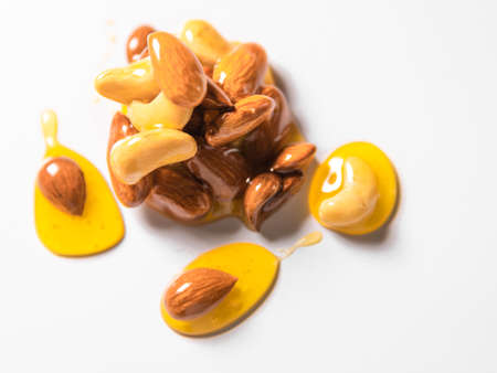 Honey drops mixed with nuts spilled on white surface.の写真素材