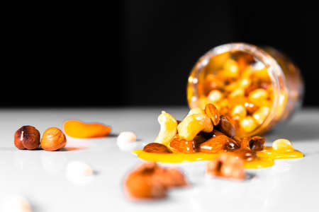 Closeup jar of honey mixed with nuts spilled on white table on black background.の写真素材