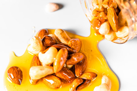 Closeup jar of honey mixed with nuts spilled on white table on black background.の写真素材