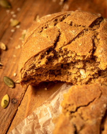 Close-up broken homemade fresh bread and pumpkin seeds on parchment paper the wooden table.の写真素材