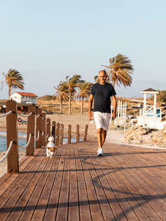 Athletic 60-years old man walking together with his dog jack russell terrier by the seaの写真素材