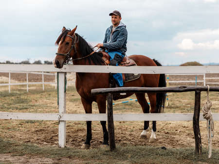 Rider riding bay horse on village background with old wooden millの写真素材