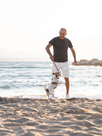 Elderly perso and his dog have fun playing by the sea.の写真素材
