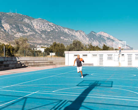 60-years old basketball player runs on playground to shoot sport ballの写真素材