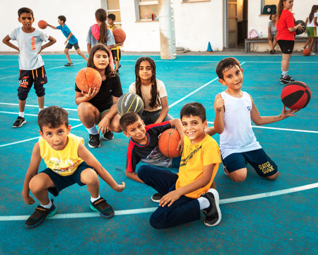 Northen Cyprus, Girne, Alsancak - Jule, 25, 2023: Basketball sports training for children teenagers around 7-14 years old. The boys and girs sitting down with balls on a basketball court in summer.のeditorial素材