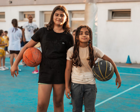 Northen Cyprus, Girne, Alsancak - Jule, 25, 2023: Two happy girls with balls on basketball sport training for teenagers around 7-14 years old on a basketball court outside at summer.のeditorial素材