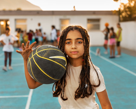Northen Cyprus, Girne, Alsancak - Jule, 25, 2023: Basketball sport training on a basketball court outdoors. Portrait of 12-yars old girl with african braids running with ball and looking camera.のeditorial素材