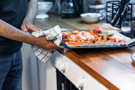 Senior Man Taking Roasted Vegetables and Shrimp Tray Out of the Oven at Homeの写真素材