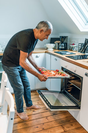 Senior Man Cooking Healthy Vegetables at Home in Modern Kitchenの写真素材