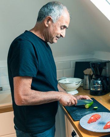 Senior Man Slicing Fresh Cucumber in Modern Attic Kitchenの写真素材
