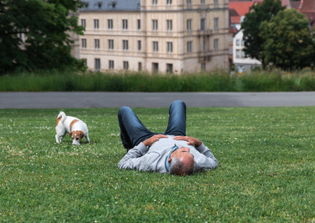 Healthy senior man resting on lawn in Coburg Hofgarten with dog nearby and Ehrenburg Palaceの写真素材