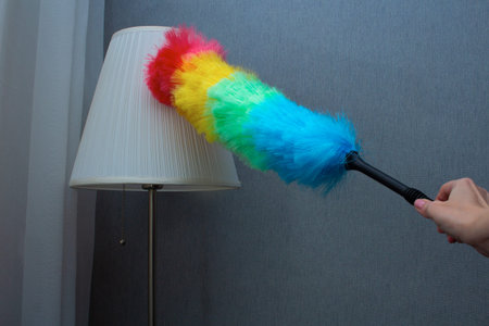 Close up of rainbow feather duster removing dust from floor lamp shade in minimalist room interiorの写真素材